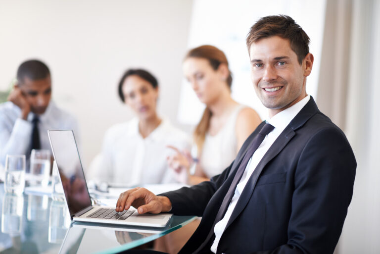 A happy corporate professional with his colleagues brainstorming in the background.
