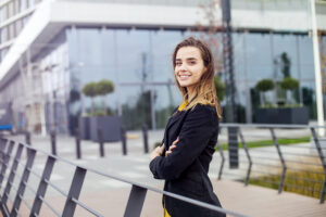 A smiling young professional standing outside an office building with her arms crossed.